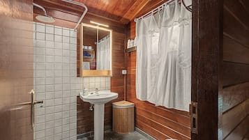 Een badkamer met een houten inrichting, een witte wastafel, een spiegel en een douche.