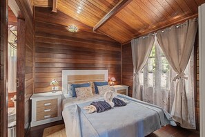 Une chambre à coucher aux murs lambrissés, avec un lit, deux tables de chevet et une fenêtre avec des rideaux.