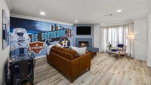 A living room with a brown sofa, a glass coffee table, a fireplace, and a wall mural.
