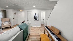 A room with a white sofa, a green blanket, a wooden bench, a piano, and a framed picture on the wall.