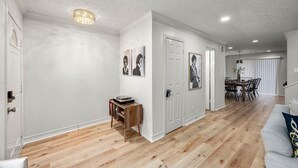 A spacious living room with hardwood flooring, a white wall, and a dining area with a table and chairs.