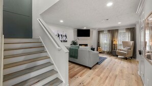 A modern living room with a fireplace, a sofa, a chair, and a staircase.