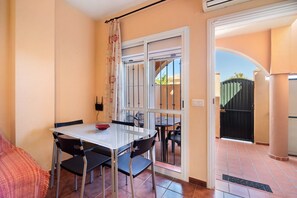 Un coin repas avec une table et des chaises, une fenêtre avec un rideau et une porte donnant sur l’extérieur.