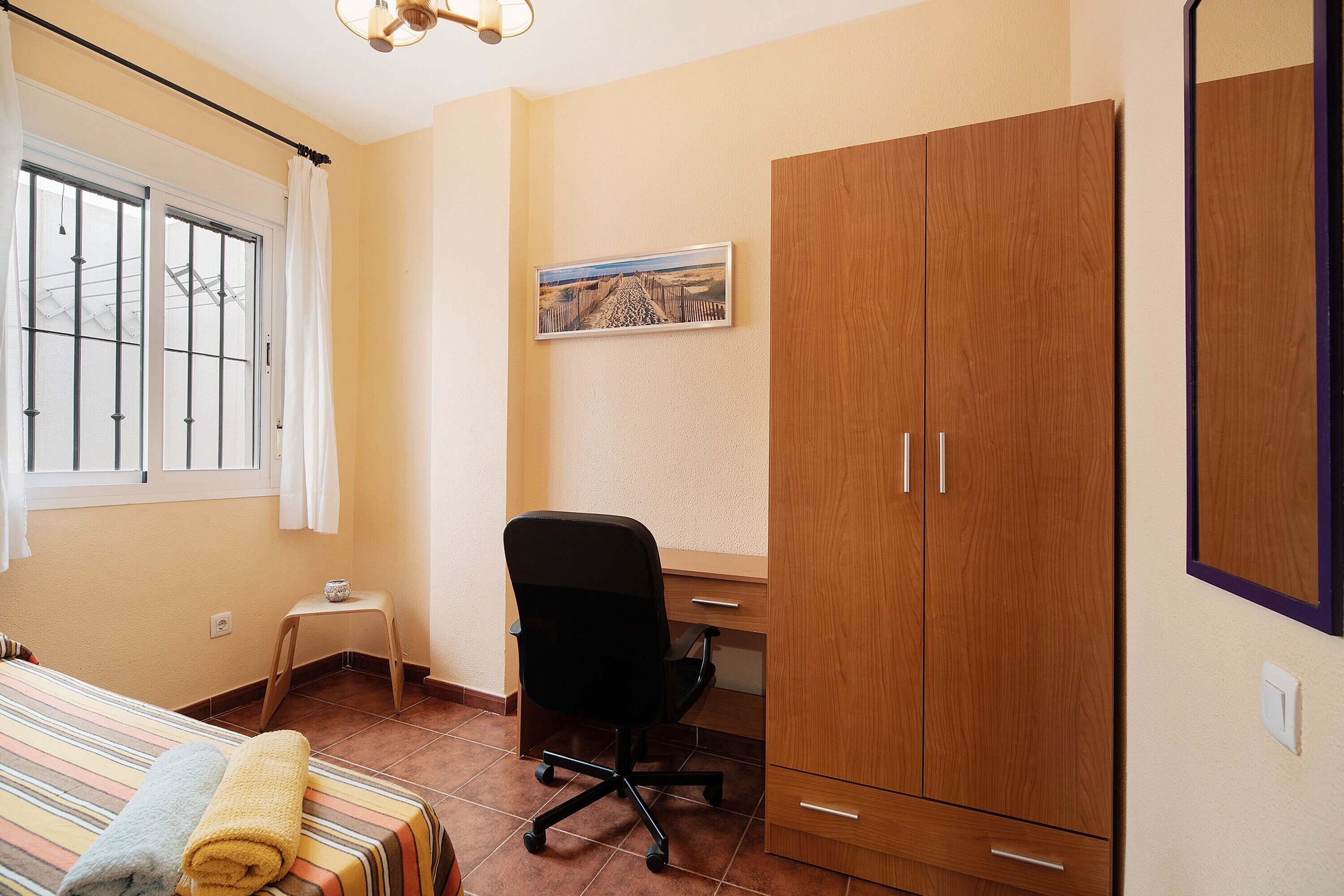 Une chambre à coucher comprenant un lit, un bureau, une chaise, une armoire et une fenêtre avec des rideaux.