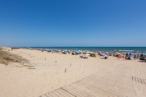 Une plage avec une promenade en bois, des parasols et des gens.