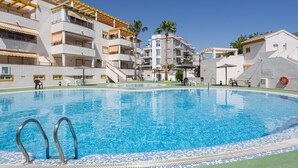 A swimming pool with a tiled edge, surrounded by multi-story buildings with balconies and outdoor seating. - Holiday Home 'Casa Fran' with Sea View, Shared Pool and Air Conditioning (Oliva)