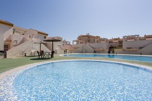 Una piscina con borde de azulejos, rodeada de edificios con balcones y un cielo despejado.