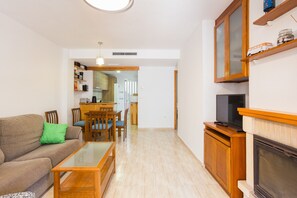 Una sala de estar con sofá, mesa de centro, televisor, chimenea y una cocina al fondo.
