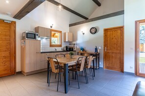 Une cuisine moderne avec des meubles en bois, une table à manger avec des chaises, un four à micro-ondes et une horloge au mur.