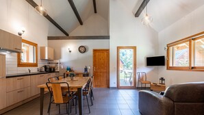 Una cocina amplia con armarios de madera, una mesa de comedor y sillas. Hay un televisor montado en la pared y una puerta que da al exterior.