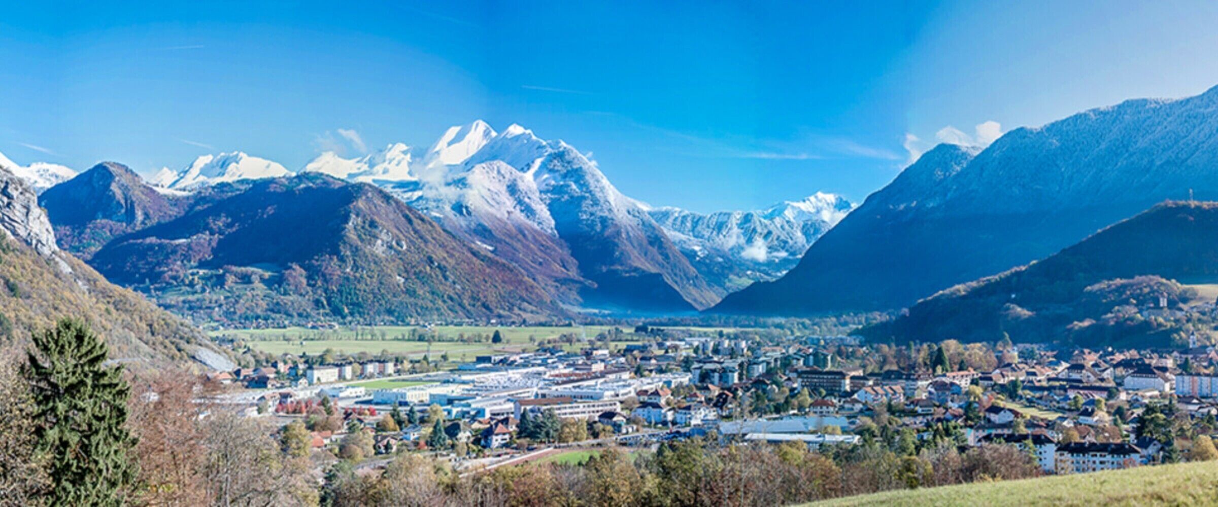 Une ville nichée entre des montagnes, avec des sommets enneigés en toile de fond.