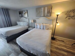 Habitación de hotel con dos camas, una mesita de noche con lámpara, una obra de arte en la pared y una lámpara de pie.