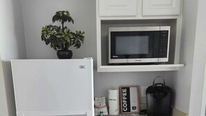 Uma cozinha compacta com geladeira branca, micro-ondas, cafeteira Keurig e um pequeno vaso de planta.