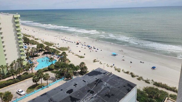 Vista da praia com piscina, palmeiras e um edifício de hotel.