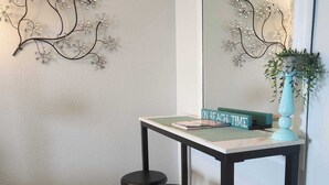 Quarto com escrivaninha, três banquinhos pretos, espelho, um ornamento na parede e um aviso que diz 'MODO PRAIA'.