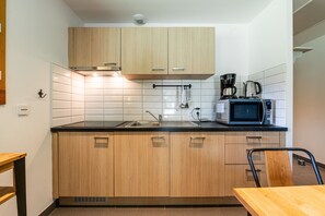 Une cuisine avec des meubles de rangement en bois, un plan de travail noir, un four à micro-ondes, une machine à café et un évier.