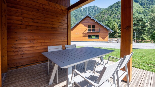 Een houten chalet met een balkon, een tafel met stoelen en uitzicht op een berg.