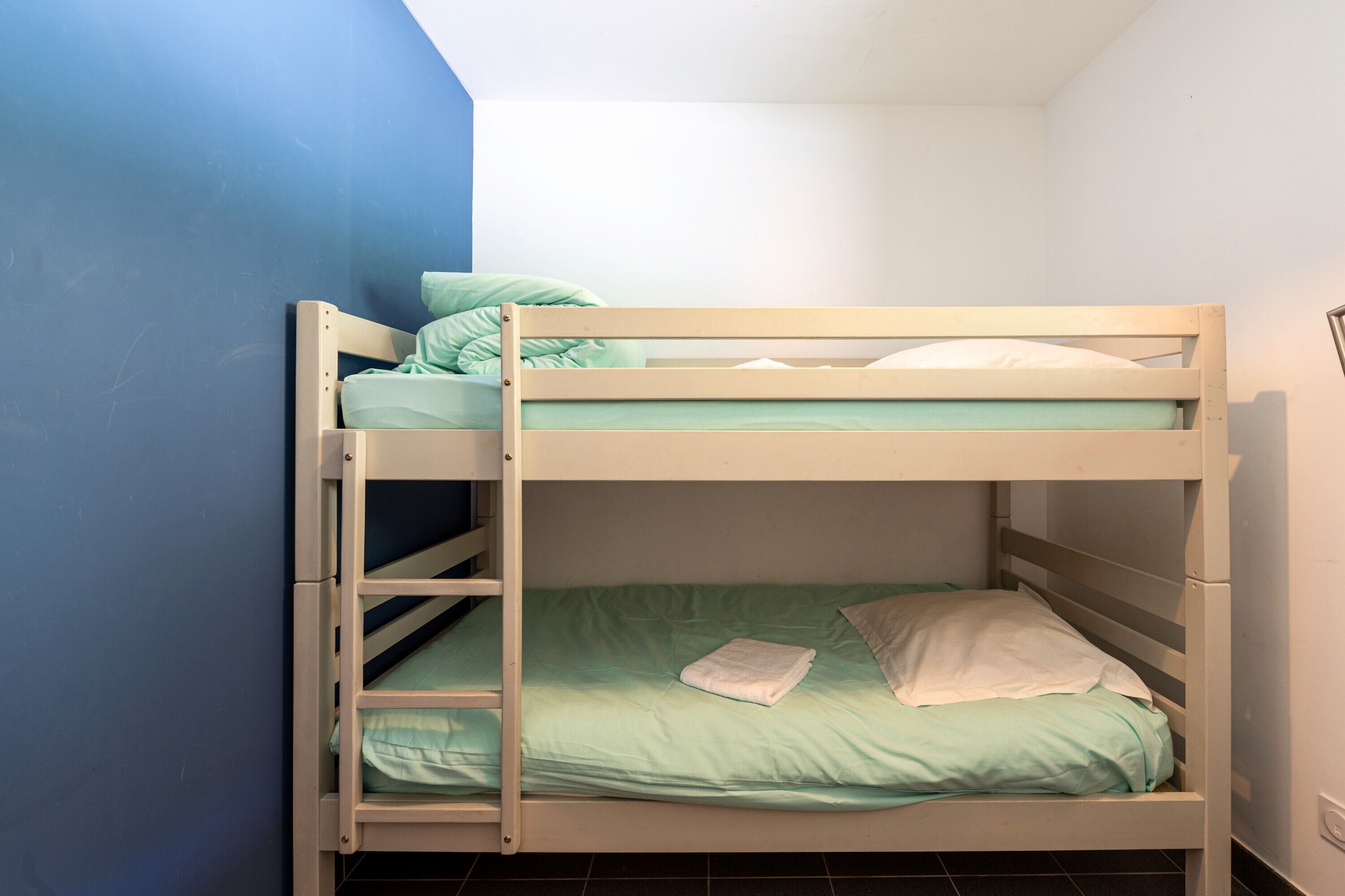Ein Stockbett mit einer Leiter, ein Einzelbett darunter und ein Kissen im unteren Bett.
