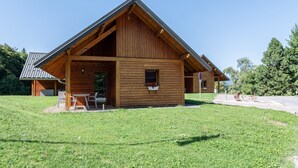 Een houten chalet met een schuin dak, een veranda met stoelen en een raam met bloemen.