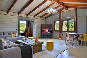 A spacious living room with a sofa, coffee table, and a TV. There are yellow ottomans and a dining area with chairs.