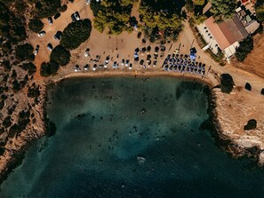 Vista aérea de una playa con una extensa masa de agua cristalina, un área de estacionamiento con automóviles y un edificio de techo rojo.