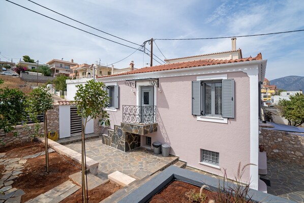 Una casa rosa con balcón, escalones de piedra y un jardín.