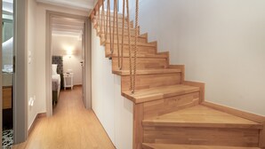 Un escalier en bois avec une rampe en corde, menant à une chambre à coucher équipée d’un lit et d’une table de chevet.