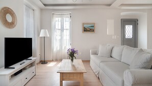 Un salon avec un téléviseur à écran plat, une table basse ornée d’un vase de fleurs, un canapé, une lampe et un tableau accroché au mur.