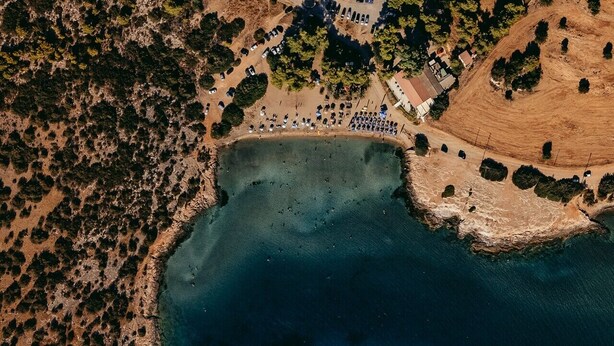 Une vue aérienne d’une zone côtière avec une plage, des voitures garées et quelques bâtiments.