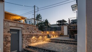 Un escalier en pierre mène à une terrasse en bois, agrémentée d’un éclairage extérieur, et est entouré d’un mur de pierre et d’une porte.
