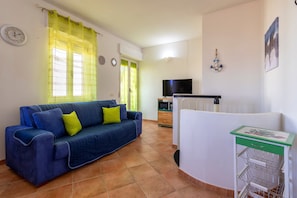 A living room with a blue sofa, a TV, a kitchen area, and a green and white cart.