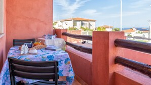 Un balcon avec une table dressée pour deux personnes, une chaise, une nappe blanche et une vue sur les bâtiments en arrière-plan.