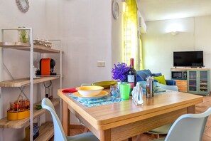 Un coin repas avec une table en bois, des chaises, un téléviseur et une cuisine en arrière-plan.