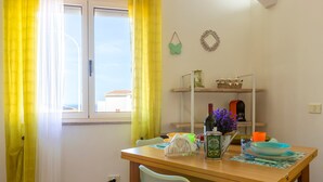 Un coin repas comprenant une table, des chaises, une étagère avec des objets décoratifs et une fenêtre avec des rideaux.