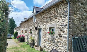 Un edificio de piedra con diseño tradicional, que presenta una pequeña entrada y ventanas con macetas de flores.