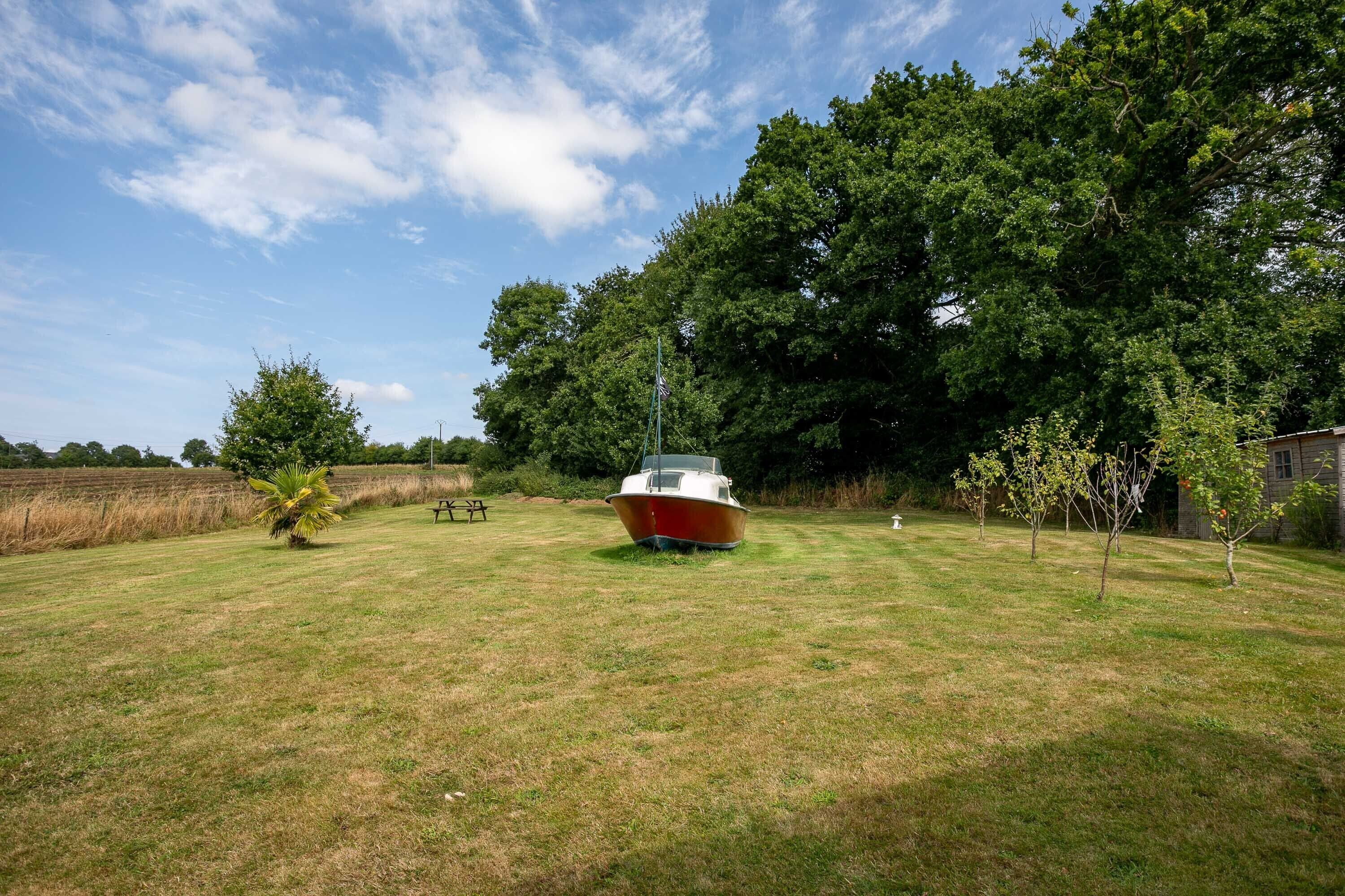 A boat in a grassy area with trees and a building in the background.