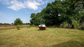 A boat in a grassy area with trees and a building in the background.