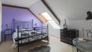 Een slaapkamer met een schuine kap, dakraam, een bed, een dressoir, een lamp en een glazen tafeltje.