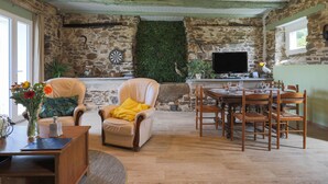Een rustiek interieur met stenen muren, een open haard, een eethoek met houten meubels en een televisie.