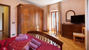 A bedroom with a bed, wooden wardrobe, television, and a chair.