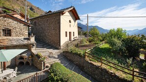 A stone building with a balcony, a wooden fence, and a view of mountains.