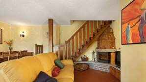 A living room with a yellow sofa, a wooden staircase, a fireplace, and a dining area.