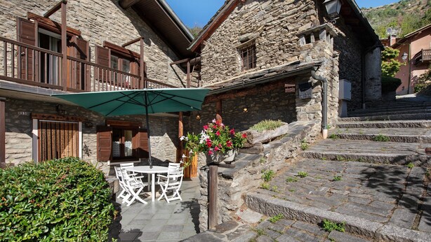 A stone building with a patio area, outdoor seating, and a staircase leading to the entrance.