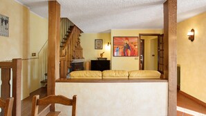 A living room with a wooden staircase, a sofa, a fireplace, and a painting on the wall.