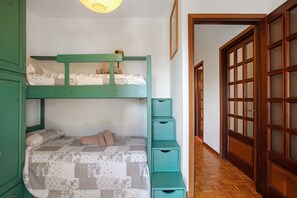 Una cama de literas con colcha, un armario verde y una puerta de madera con paneles de vidrio.