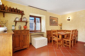 Una cocina con armarios de madera, una mesa de comedor con sillas, un ventanal con cortinas de encaje y un radiador.