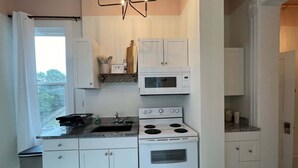 A kitchen with white cabinets, a stove, a microwave, and a window with curtains.
