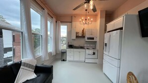 A compact living space with a sofa, a dining table, a kitchen area with white appliances, and a ceiling fan.