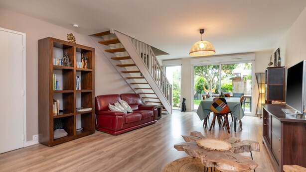 A spacious living area with a wooden staircase, a red leather sofa, a dining table, and a TV. - Holiday Home 'Upton 2 - Arradon Golfe Du Morbihan' with Private Terrace, Garden & Wi-Fi (Arradon)