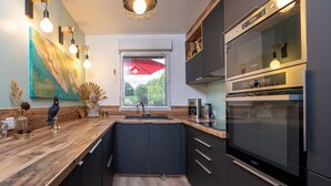 A modern kitchen with a built-in oven, a large window with blinds, and a wooden countertop. - Holiday Home 'Upton 2 - Arradon Golfe Du Morbihan' with Private Terrace, Garden & Wi-Fi (Arradon)